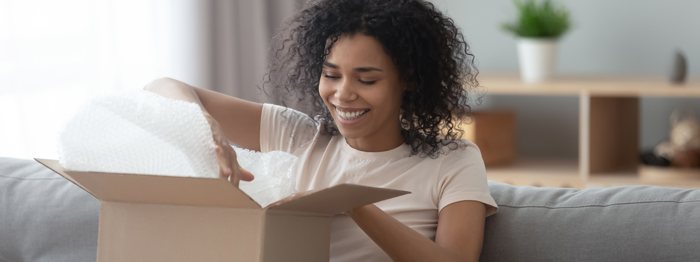 A person opening a box on a living room sofa.